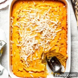 A white baking pan of baked corn souffle with a piece cut out and a spoon in the lower right side.