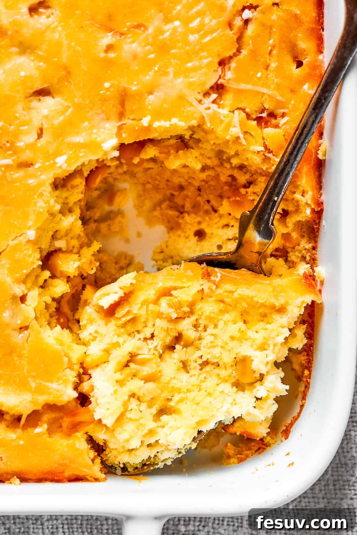 Golden Cloud Corn Souffle 9 A spoon scooping a generous portion of warm, creamy corn souffle from a baking dish.