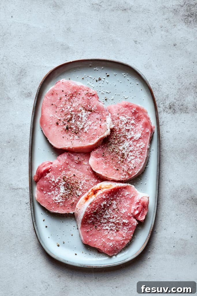 Pork chops seasoned with salt and pepper on a white tray, ready for cooking.