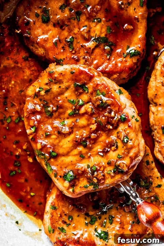 Close-up image of a spoon holding up a cooked honey garlic pork chop, showing the glistening sauce.