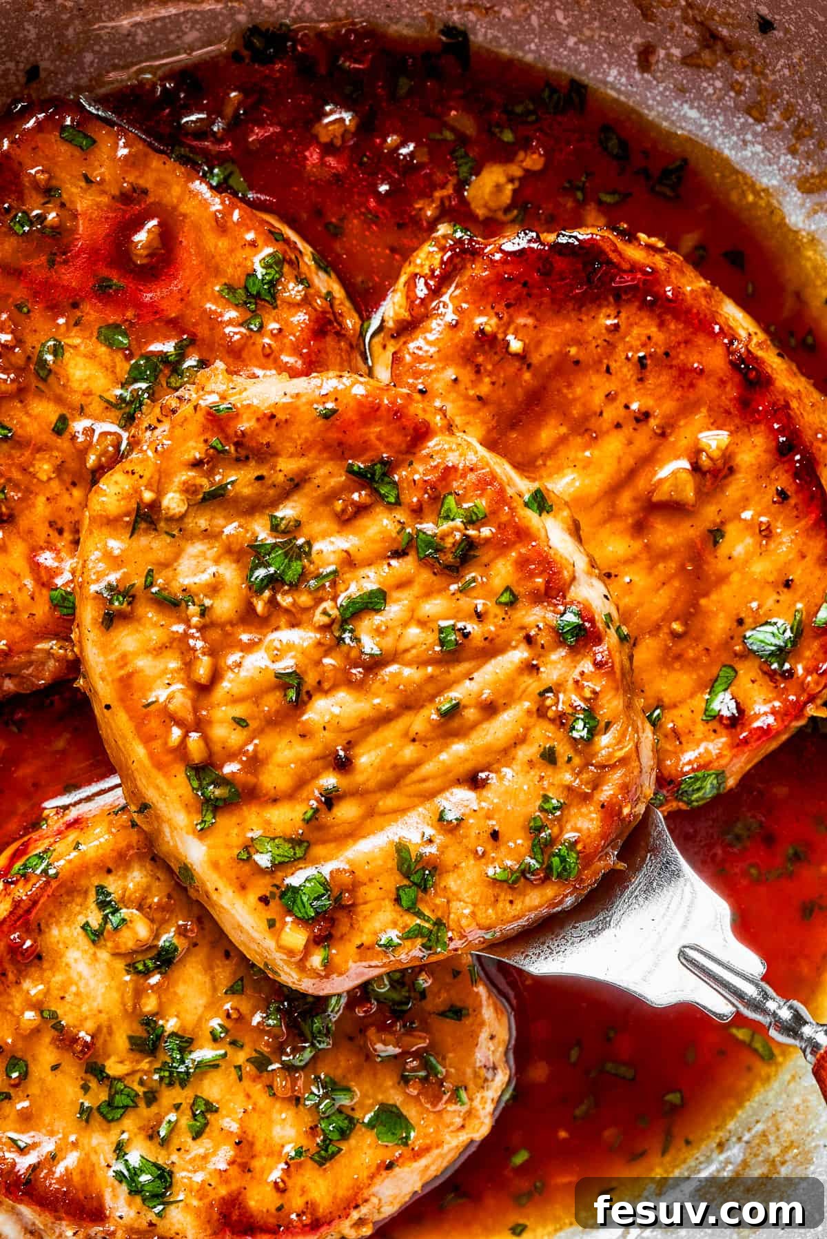 Up close view of finished honey garlic pork chops, coated in a sticky sauce and garnished with parsley.
