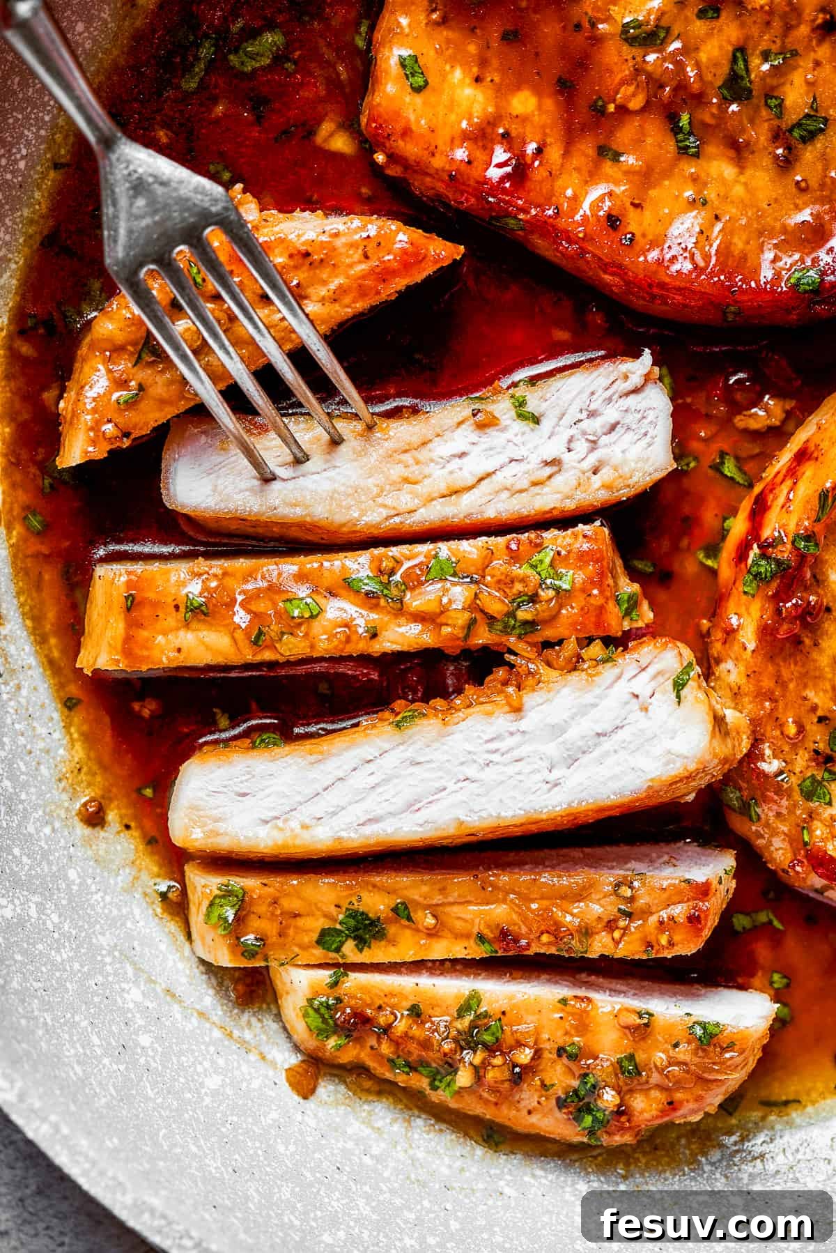Sliced pork chops with a fork reaching for a piece, showing the tender interior and glazed exterior.