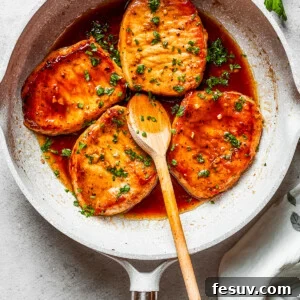 Four honey garlic pork chops cooking in a skillet with a wooden spoon stirring through.