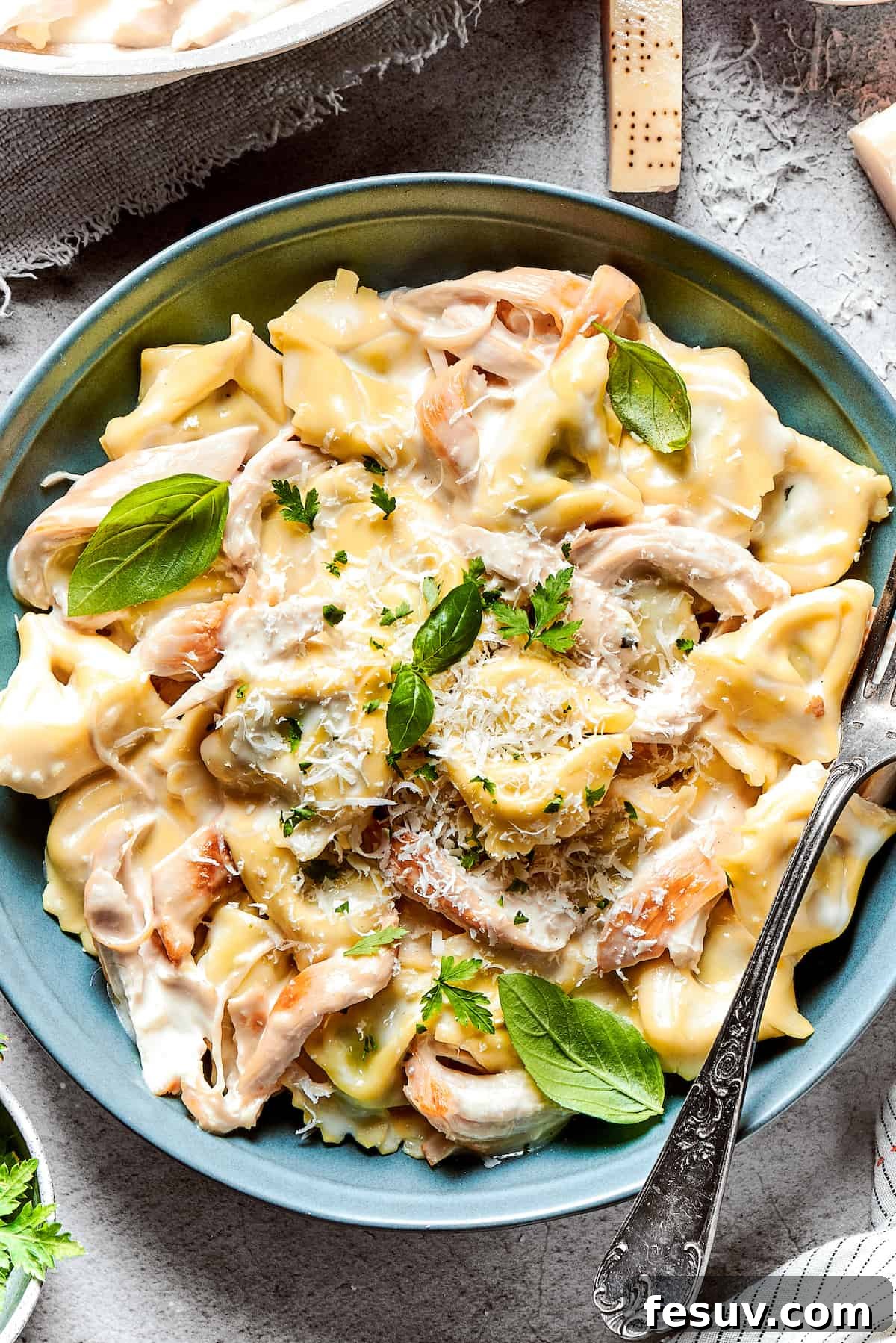 Close-up overhead shot of chicken tortellini alfredo served in a blue bowl and garnished with basil leaves.