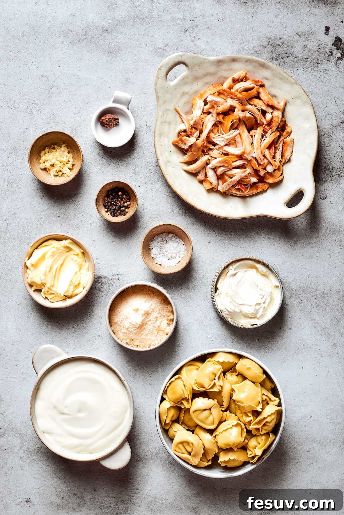 The ingredients for chicken tortellini alfredo are shown portioned out in bowls: chicken, cheese tortellini, salt and pepper, basil and parsley, heavy cream, butter, cream cheese, garlic, nutmeg.