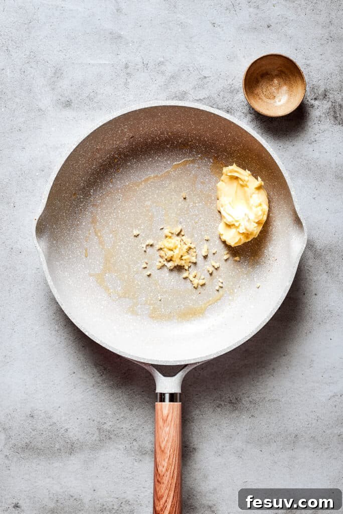 A white skillet holds butter and chopped garlic.