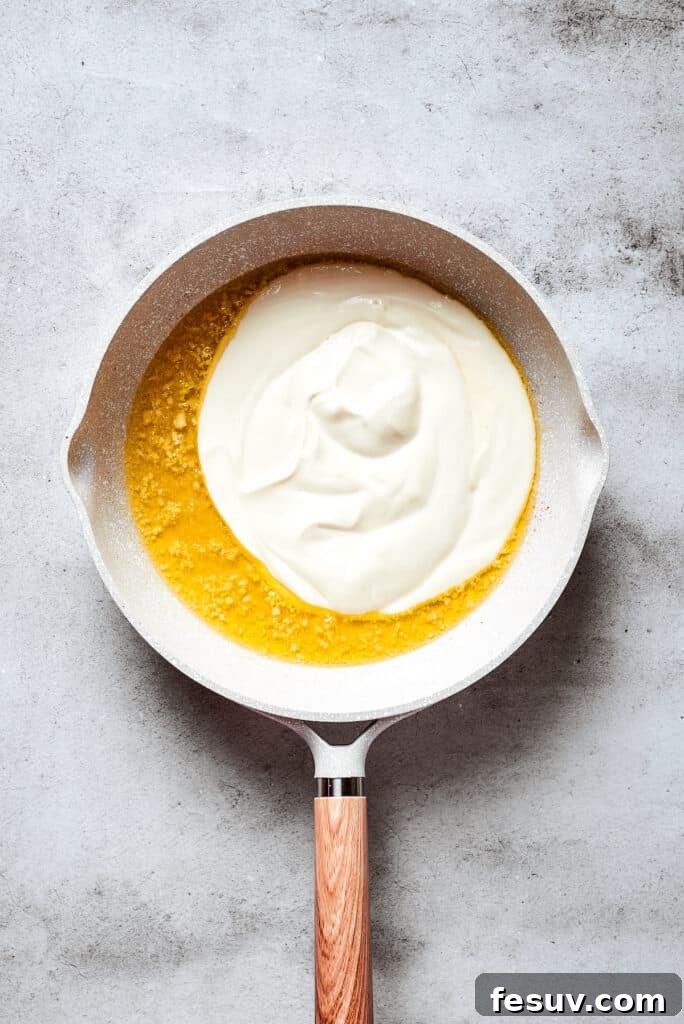 Cream cheese and heavy cream sit on top of melted butter with garlic in a white skillet.