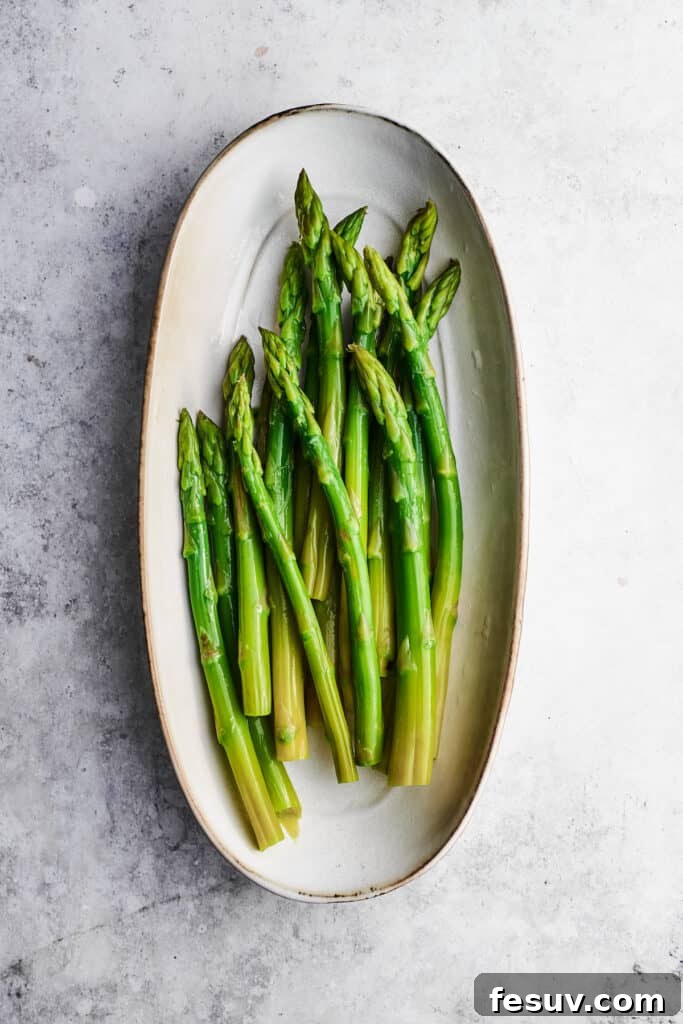 Preparing fresh asparagus for Chicken Madeira by blanching. Fresh asparagus spears ready for blanching in an oval white baking dish.