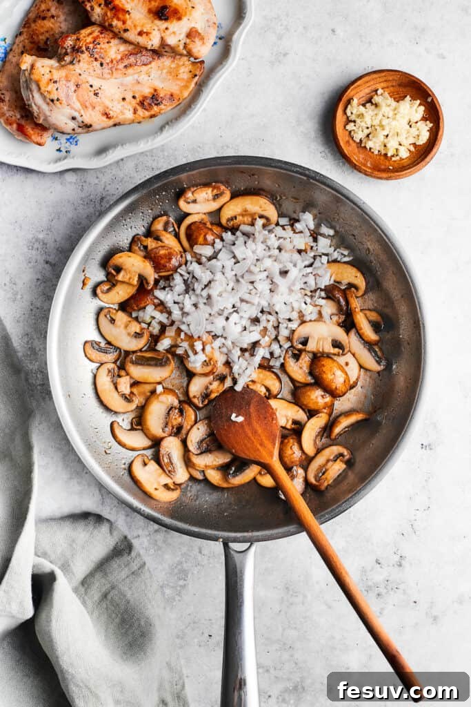 Adding garlic to sautéed mushrooms for the Chicken Madeira sauce base. Minced garlic is added to a skillet of cooking mushrooms with a wooden spoon, enhancing the aroma.