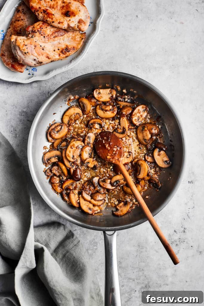 Perfectly sautéed mushrooms for a rich, flavorful sauce. A wooden spoon stirs a metal skillet full of cooked sliced mushrooms, perfectly browned and tender.