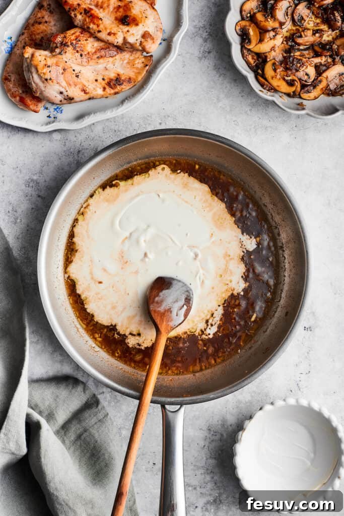 Adding heavy cream to thicken the Madeira sauce. A wooden spoon stirs in heavy cream into the sauce for chicken Madeira, creating a smooth, rich consistency.