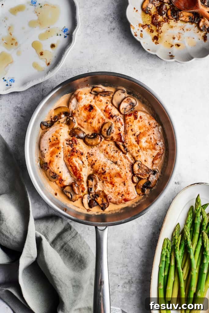 Rich and creamy Chicken Madeira sauce simmering in the skillet. A metal skillet of finished chicken Madeira with cooked chicken, sautéed mushrooms, and a bubbling cream sauce, ready for cheese.