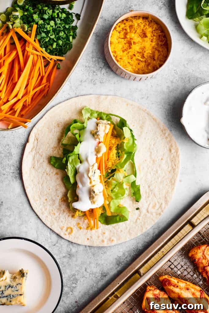 This Buffalo Chicken Wrap is packed with chicken tenders, cheese, lettuce, avocado, Ranch, and hot sauce in a warm flour tortilla. Ranch dressing is drizzled over a tortilla and vegetables to make a buffalo chicken wrap.