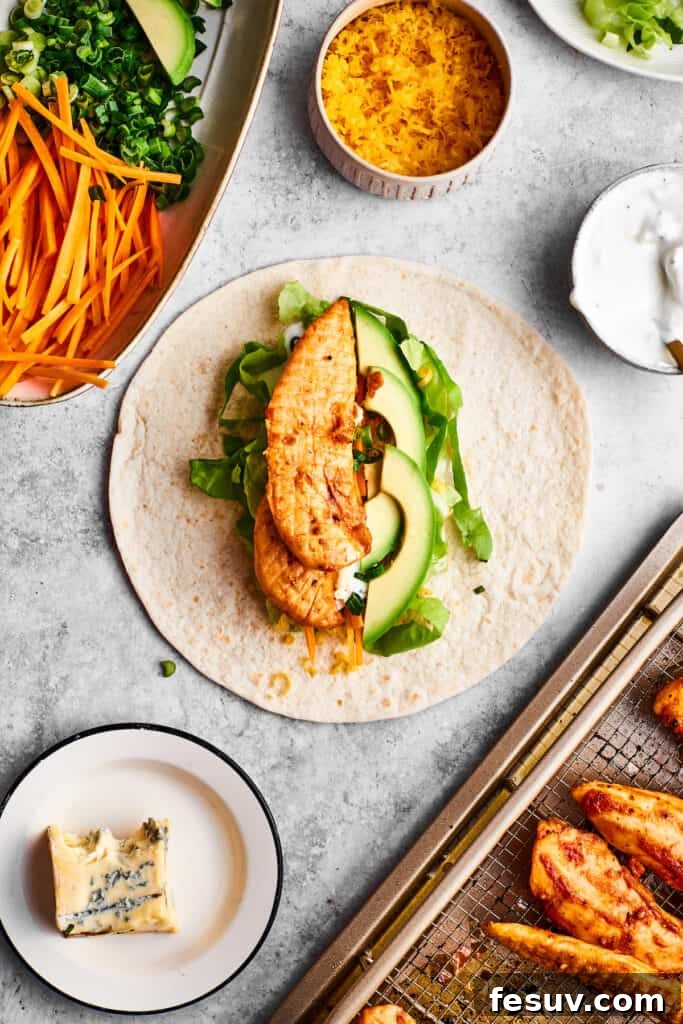 This Buffalo Chicken Wrap is packed with chicken tenders, cheese, lettuce, avocado, Ranch, and hot sauce in a warm flour tortilla. A seasoned chicken tender is placed on vegetables and a tortilla.