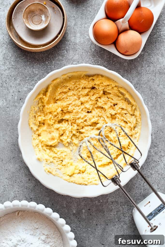 A hand mixer creams butter and sugar in a white bowl.