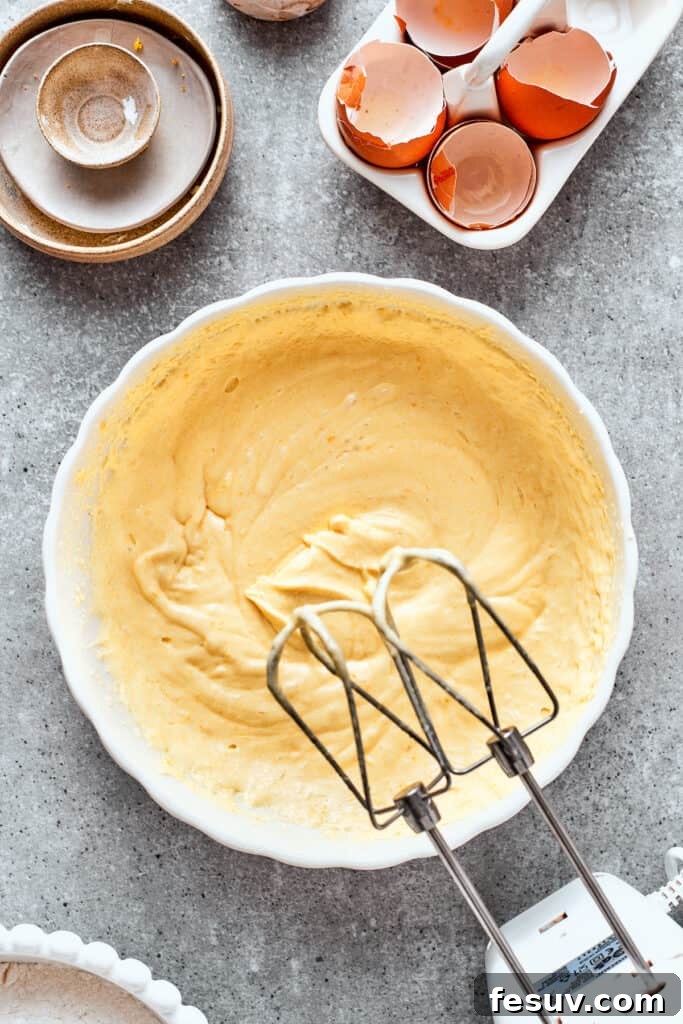 A hand mixer beats the batter for orange cake in a white bowl.