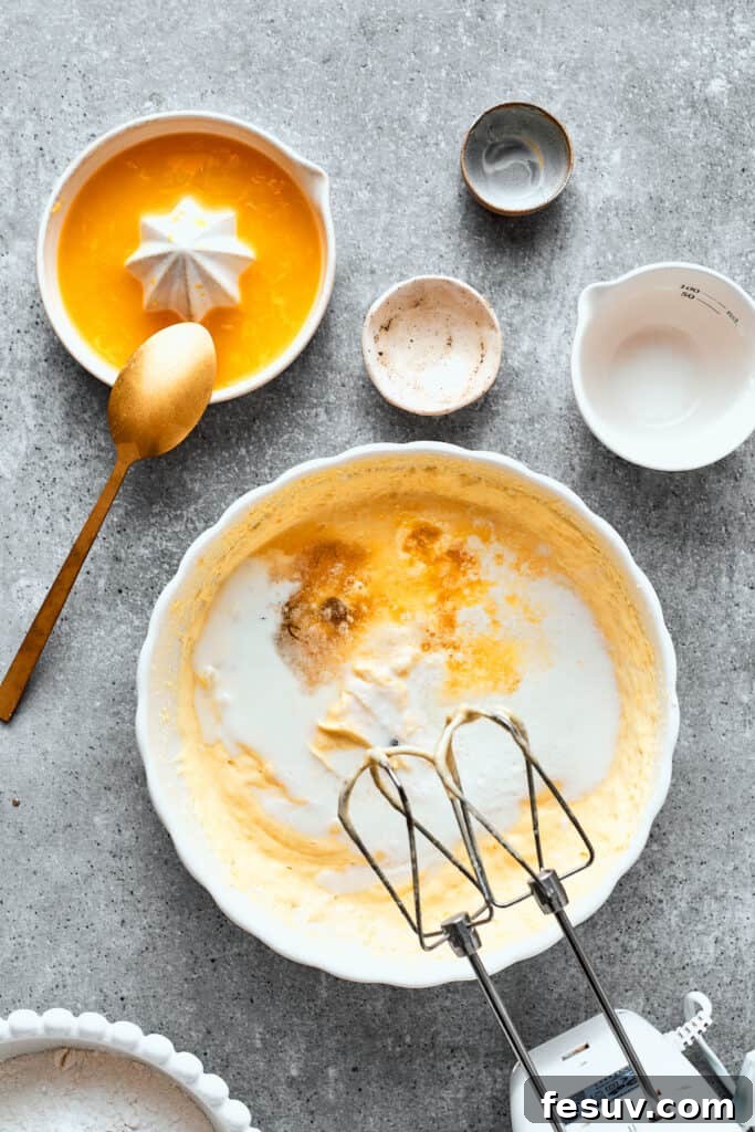 Vanilla paste and orange juice are mixed into a bowl of orange cake batter.