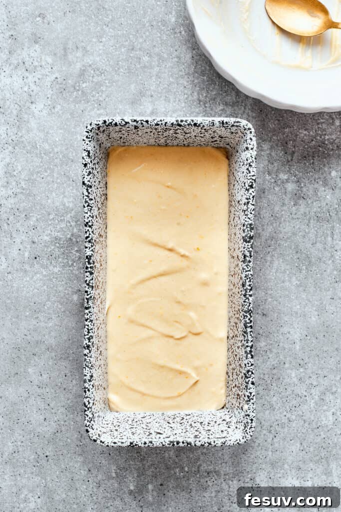 Orange cake batter is smoothed into a metal loaf pan.