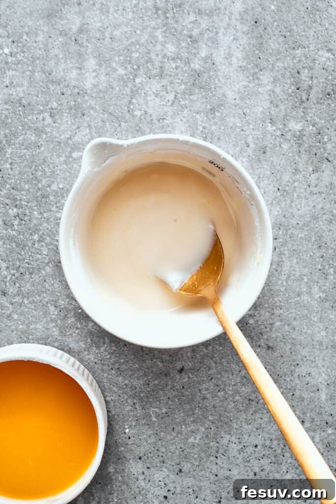 A white bowl of orange glaze is mixed with a wooden spoon.
