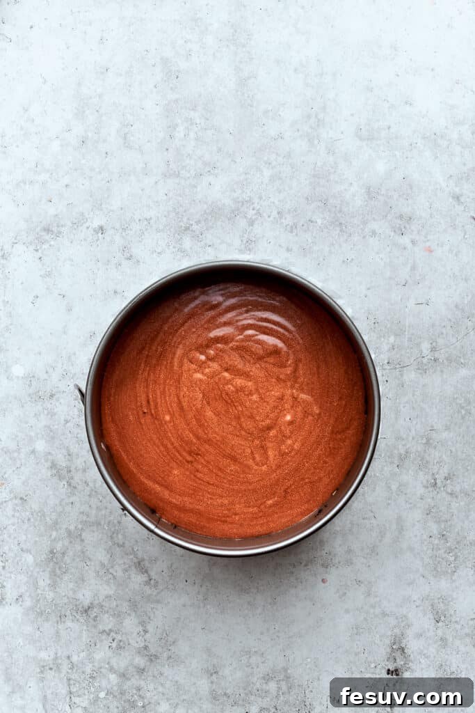 The rich chocolate cheesecake filling is being carefully spread over the caramel-pecan layer, creating a distinct and delicious second layer for the Turtle Cheesecake.