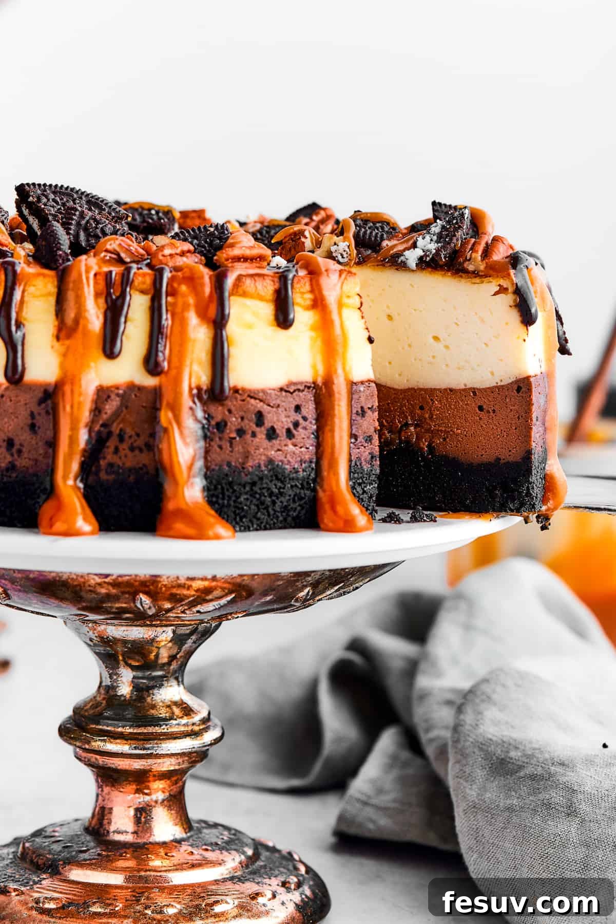 A server pulling a perfect slice of Turtle Cheesecake, showcasing its rich layers, from the whole cake on a decorative cake stand.
