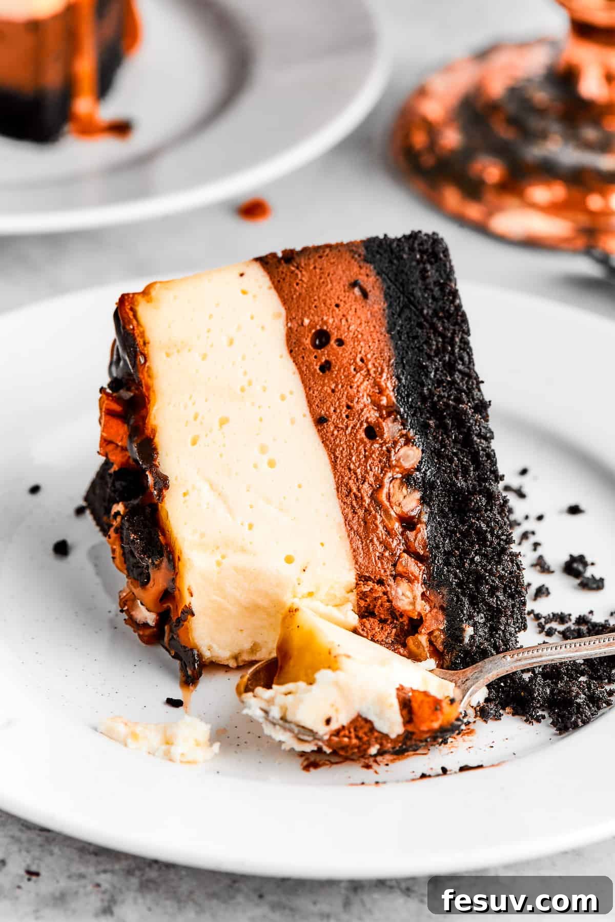 A perfect slice of Turtle Cheesecake, topped with chocolate ganache, caramel, and pecans, served elegantly on a white dessert plate.