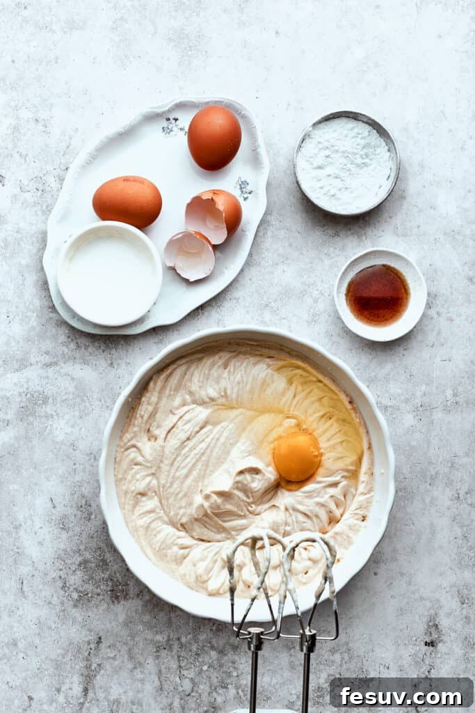 Large eggs are gently beaten into a creamy bowl of cheesecake batter, ensuring smooth incorporation for the Turtle Cheesecake filling.