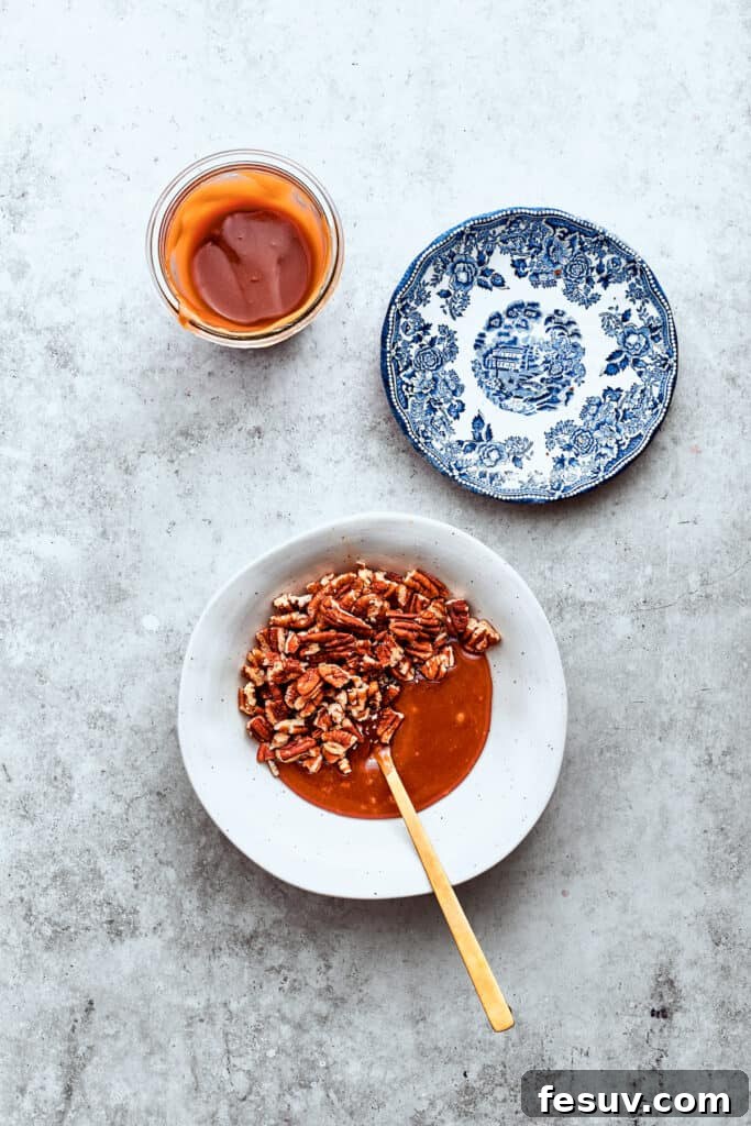 Chopped pecans and rich caramel sauce are being stirred together with a wooden spoon in a white mixing bowl, forming the luscious pecan-caramel layer for the Turtle Cheesecake.
