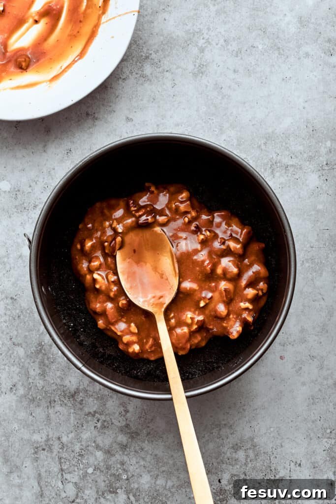 The pecan-caramel mixture is carefully spread over the chocolate cookie crust in the springform pan, establishing the rich base layer for the Turtle Cheesecake.