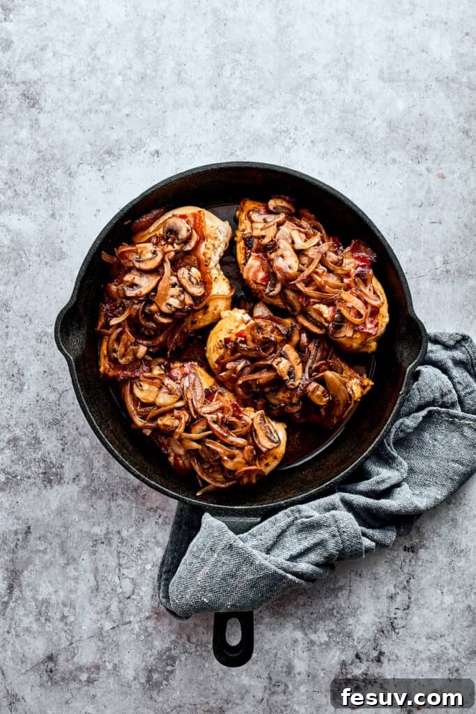 Four mushroom-topped chicken breasts in a cast iron skillet.