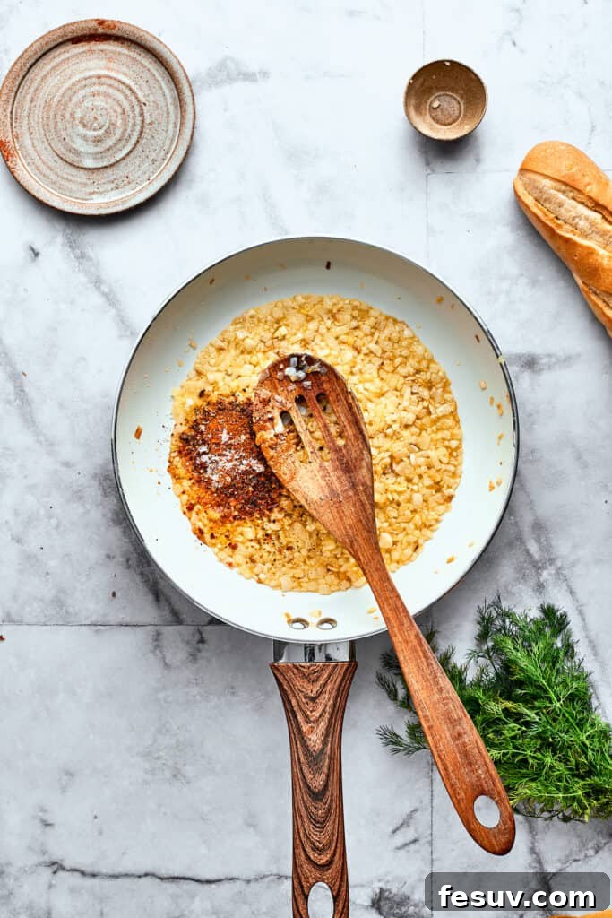 Sautéing Onions and Garlic, then Adding Tomatoes for the Sauce Base A wooden spoon carefully stirs vibrant diced tomatoes into a skillet, blending them with the softened onions and fragrant garlic.