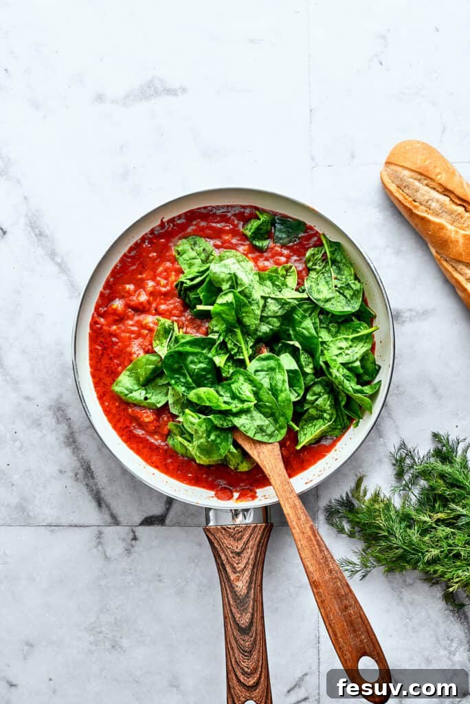 Adding Fresh Spinach to the Tomato Sauce Vibrant green spinach leaves are being thoroughly stirred into a rich, homemade tomato sauce in a skillet, adding freshness and color.