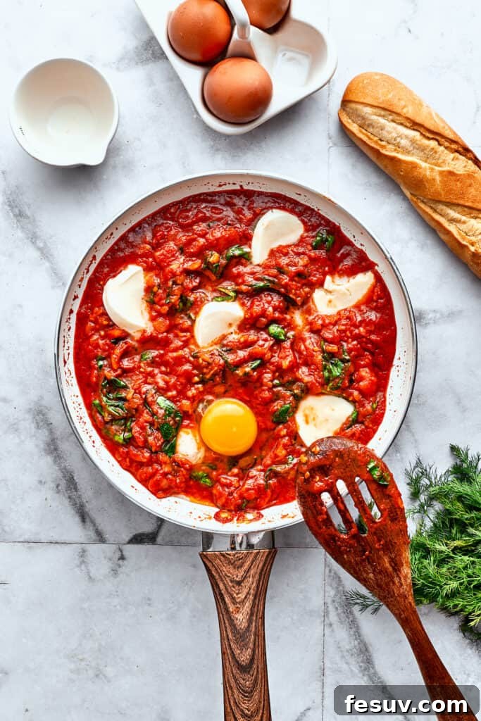 Adding Eggs to the Purgatory Sauce Cracked eggs are gently added into the prepared divots in a skillet filled with rich tomato sauce, fresh spinach, and melted cheese, ready for poaching.