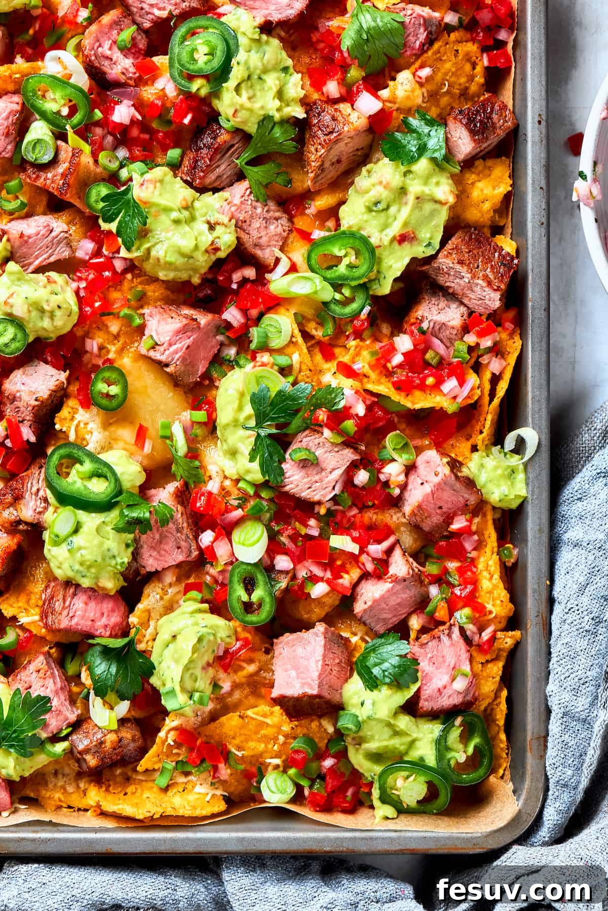 A big pan of steak nachos topped with guacamole and pico de gallo, ready to be served.