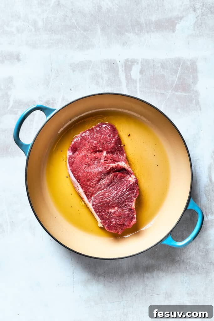A piece of steak cooks in olive oil in a pan.