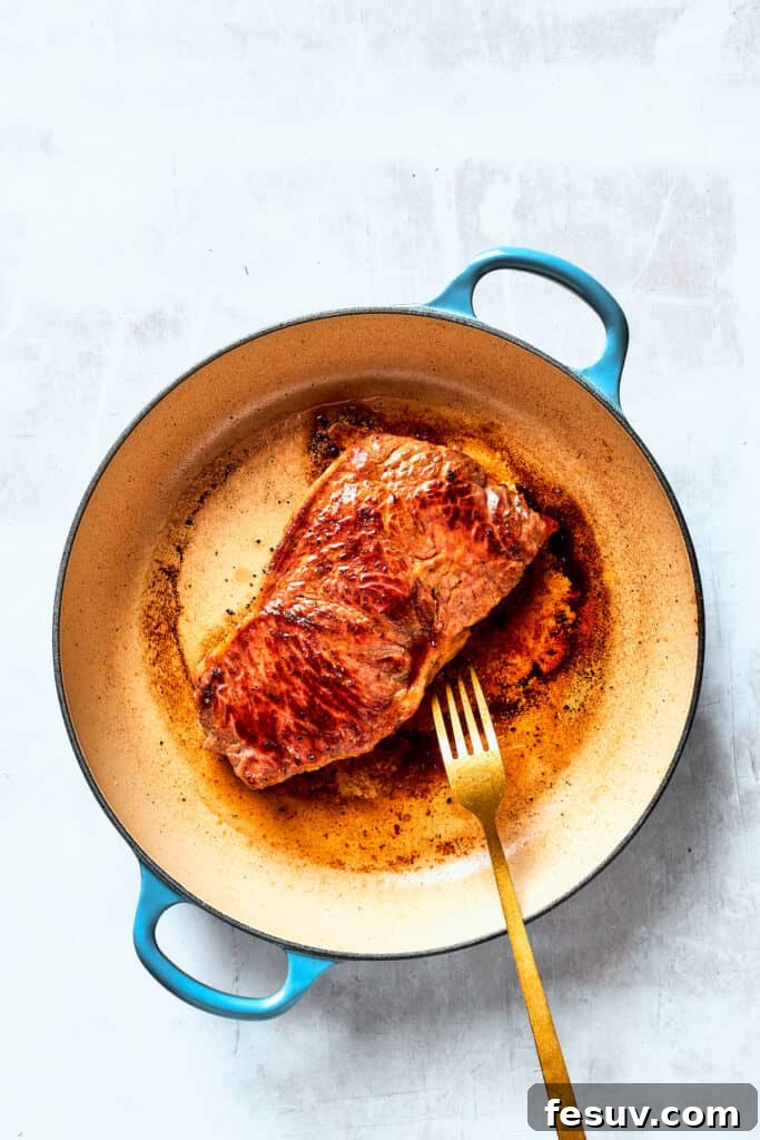 Steak is seared in a baking pan with a fork turning one of the steaks.