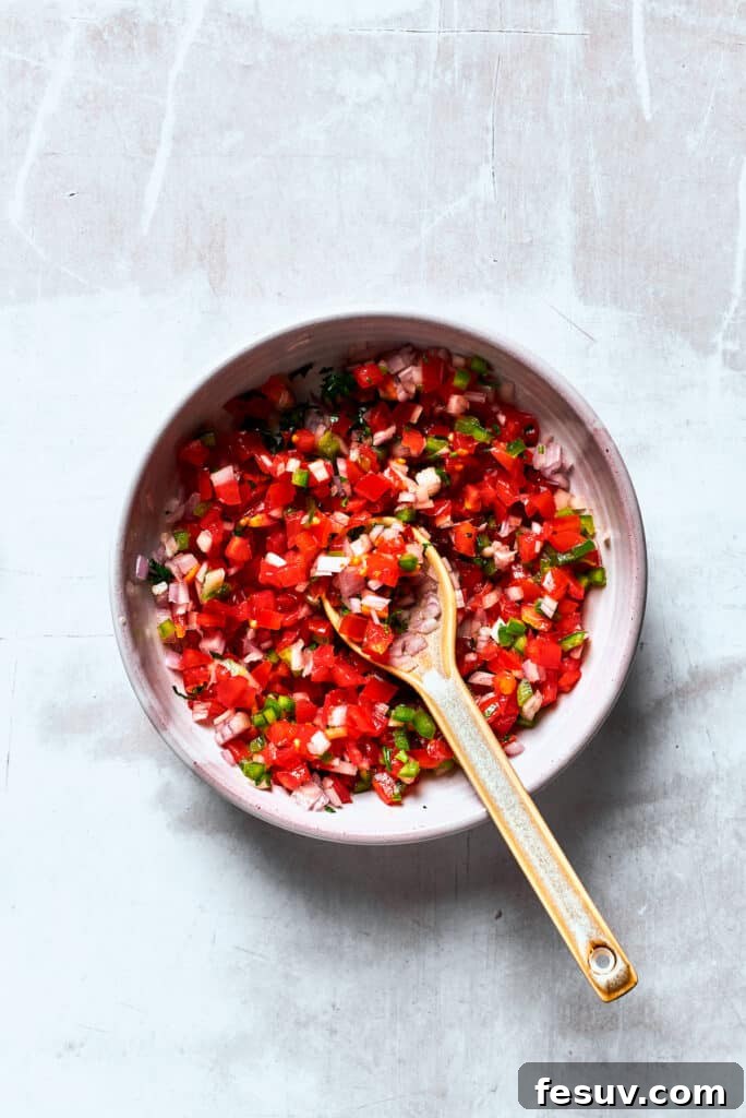 A bowl of Pico de Gallo is mixed with a wooden spoon.