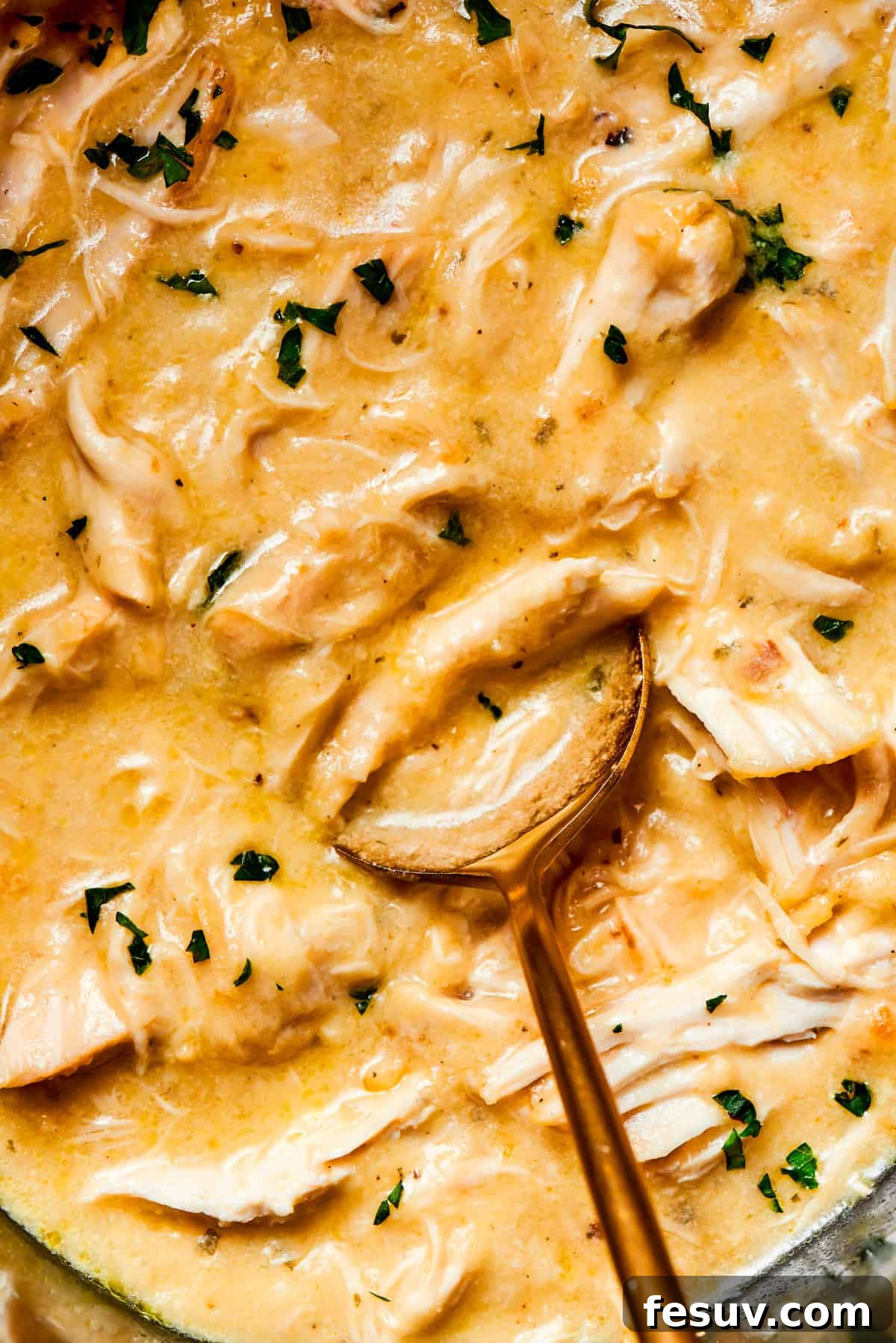 Spoon stirring through creamy sauce and shredded chicken.