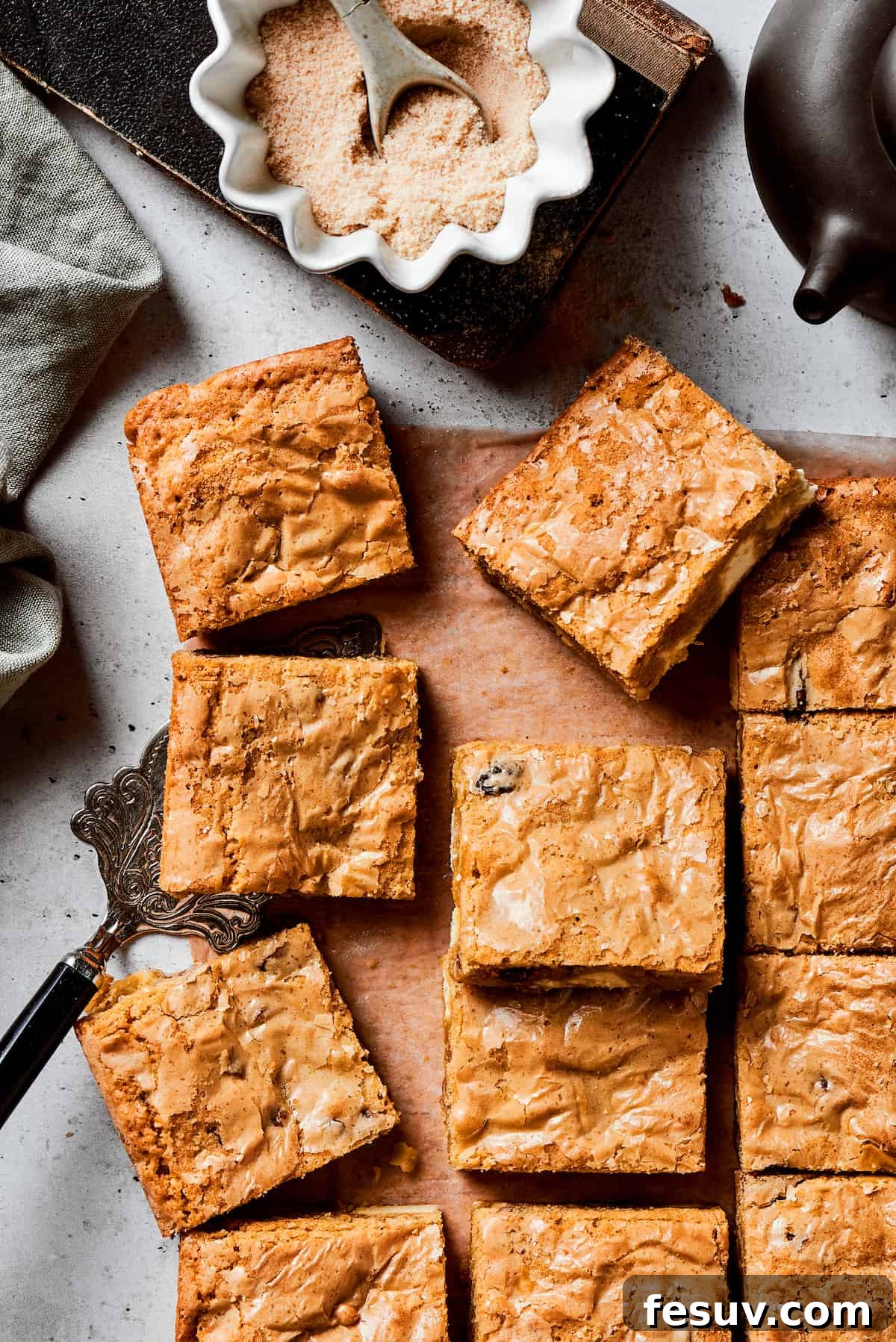 This sweet and irresistible Blonde Brownies recipe features blondies studded with white chocolate chips and crunchy pecans. A cutting board of golden blonde brownie squares with a bowl of brown sugar next to it, highlighting the chewy texture and embedded white chocolate chips and pecans.