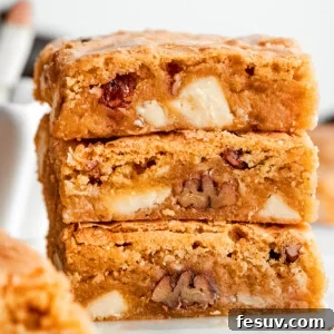 A stack of three blonde brownies with white chocolate chips and pecans visible, highlighting the rich, chewy texture.