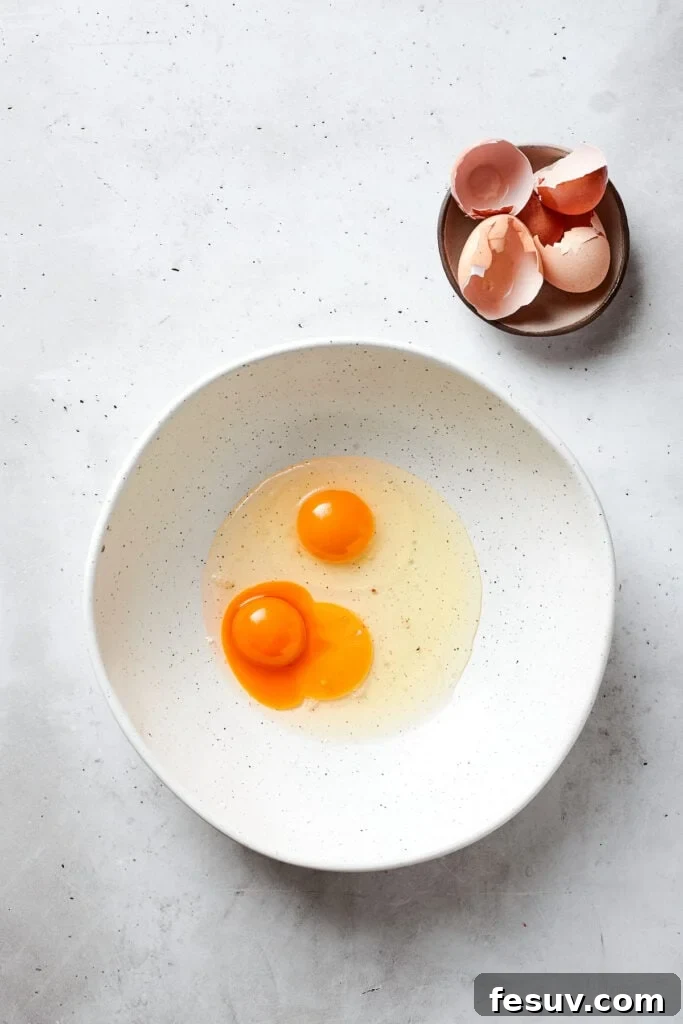 Blonde Brownies | Vanilla Blondies with White Chocolate and Pecans! Two large eggs and an extra egg yolk are shown in a white bowl, ready to be whisked for the blonde brownie batter.