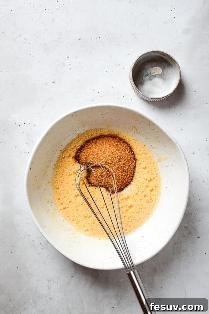 Blonde Brownies | Vanilla Blondies with White Chocolate and Pecans! Light brown sugar is gently added to a bowl containing whisked eggs, preparing for the next step of the blondie batter mixture.