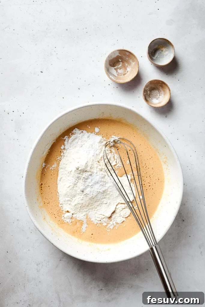 Blonde Brownies | Vanilla Blondies with White Chocolate and Pecans! The pre-mixed dry ingredients, including flour, cornstarch, baking soda, and salt, are being added to the wet blonde brownie batter in a mixing bowl.