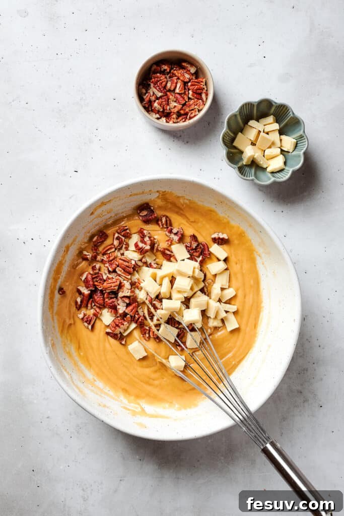 Blonde Brownies | Vanilla Blondies with White Chocolate and Pecans! Creamy white chocolate chips and crunchy chopped pecans are being folded into the smooth blonde brownies batter in a bowl, ensuring even distribution.