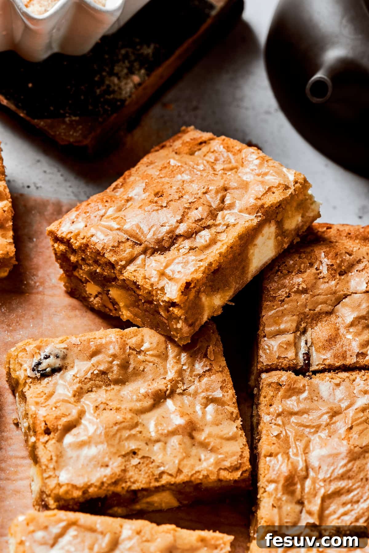 This sweet and irresistible Blonde Brownies recipe features blondies studded with white chocolate chips and crunchy pecans. A side view of a perfectly baked blonde brownie, showcasing its golden-brown top, chewy interior, and visible white chocolate chips and pecan pieces, resting on a stack of other blondies.