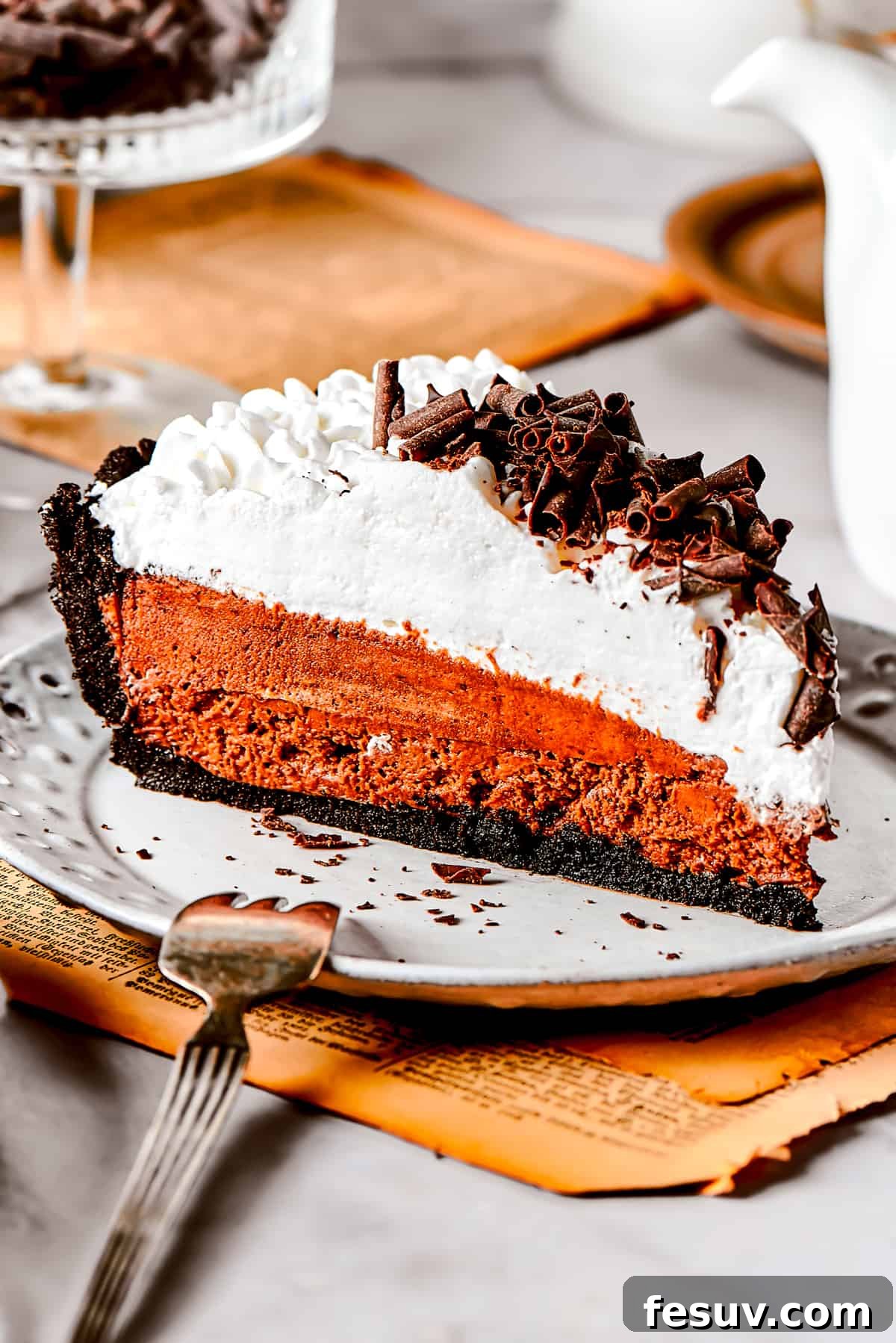A perfectly sliced French Silk Pie revealing its layers of dark chocolate filling, Oreo crust, and fluffy whipped cream, served on an elegant dessert plate.
