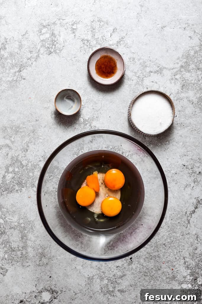 Three large eggs, granulated sugar, and water in a mixing bowl, ready to be combined.