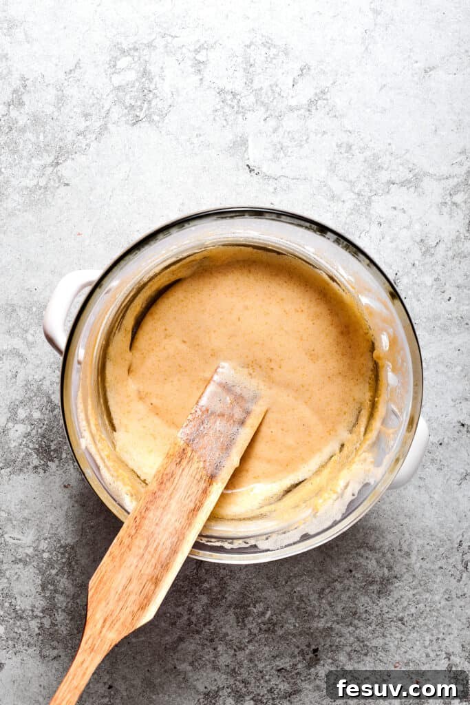 A spatula stirring the egg and sugar mixture in a bowl set over a pot of simmering water, gently cooking it.