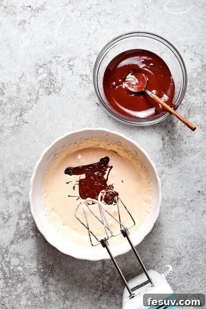 Melted chocolate being beaten into the egg and sugar mixture using a hand mixer.