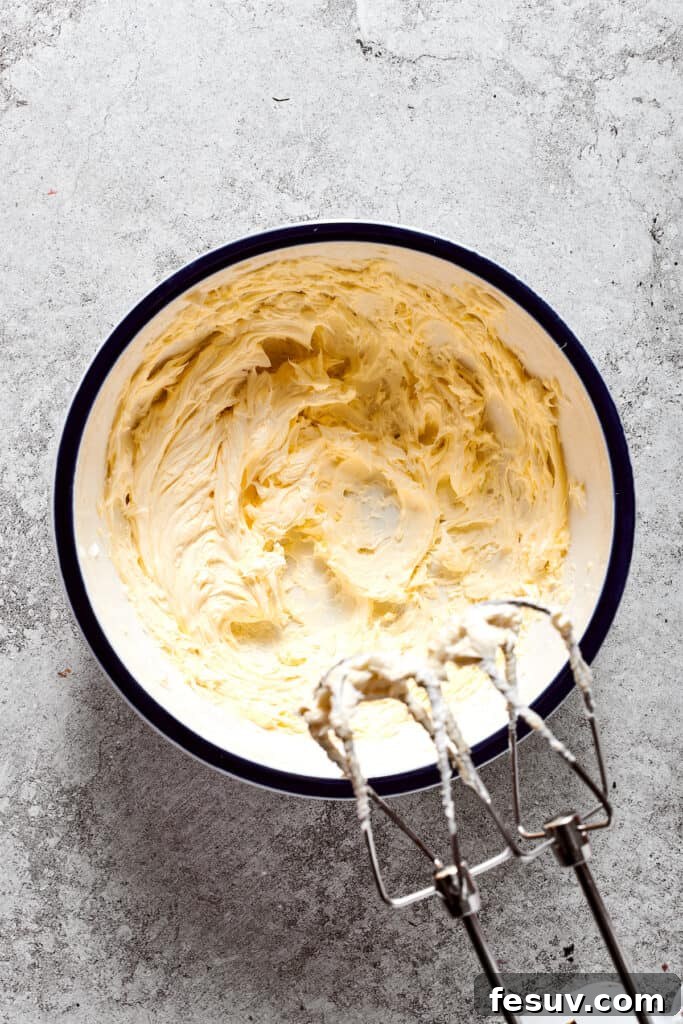 Softened unsalted butter being whipped until light and fluffy with a hand mixer.